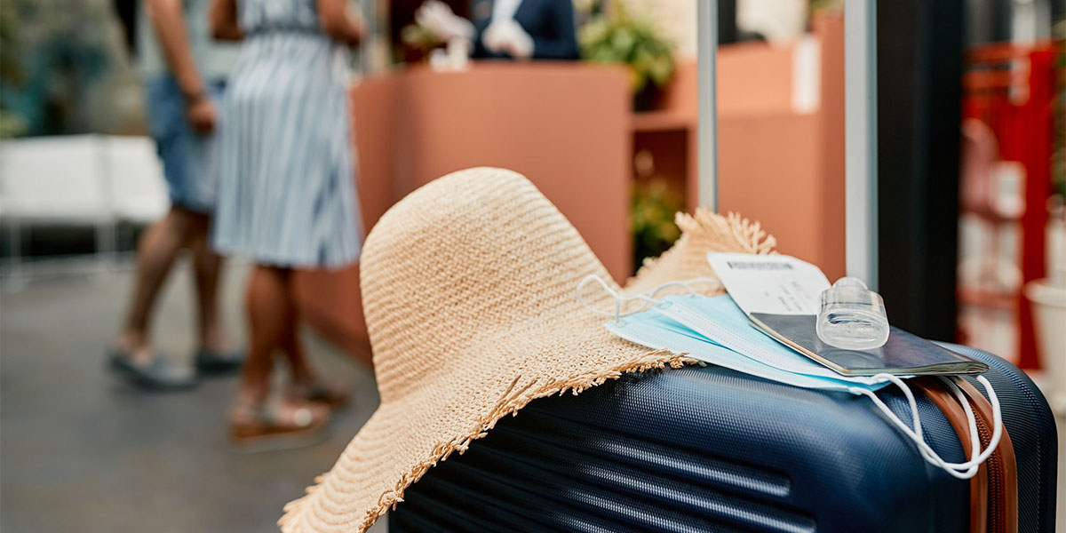 Close-up of blue suitcase with protective face mask, passport and hand sanitizer at hotel lobby