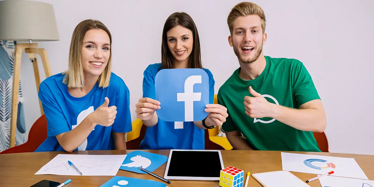 Smiling woman holding Facebook logo with her friends showing thumb up / Airbnb social media marketing on Facebook